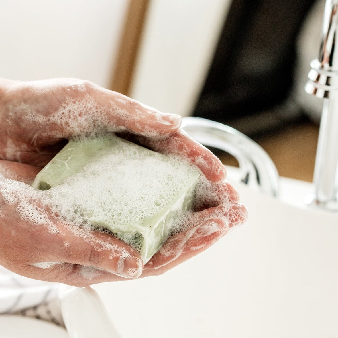 Embody Naures peppermint and pumice soap in use, lots of suds in hands over a sink
